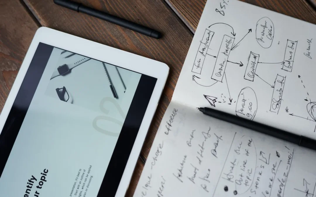 Tablette et carnet avec des notes et schémas sur une table en bois.